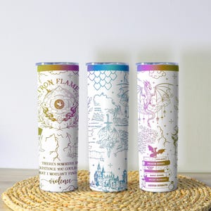 May include: Three white insulated tumblers with fantasy-themed designs. One features "Iron Flame" text and a quote about violence. Another has a map design, and the third displays a dragon and stacked books with titles like "Dragon Riders".