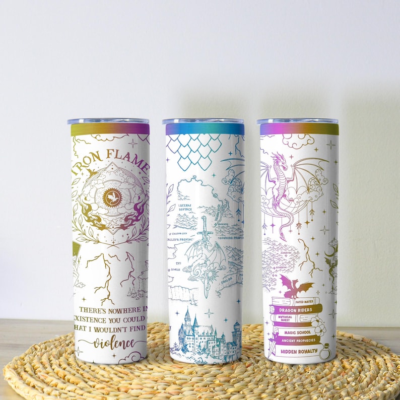 May include: Three white insulated tumblers with fantasy-themed designs. One features "Iron Flame" text and a quote about violence. Another has a map design, and the third displays a dragon and stacked books with titles like "Dragon Riders".