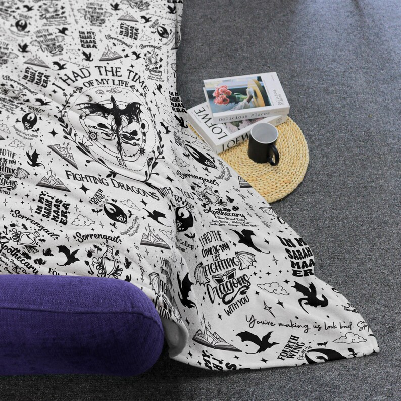 May include: White blanket with black illustrations and text, including phrases like "Fighting Dragons" and "I had the time of my life." The blanket features dragons, stars, and book graphics, with a purple bolster pillow visible.