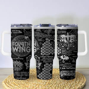 May include: Three black travel mugs with white handles and lids. Each mug features a detailed white graphic design with text, including "FOURTH WING" and dragon illustrations. The mugs are on a woven, circular mat.