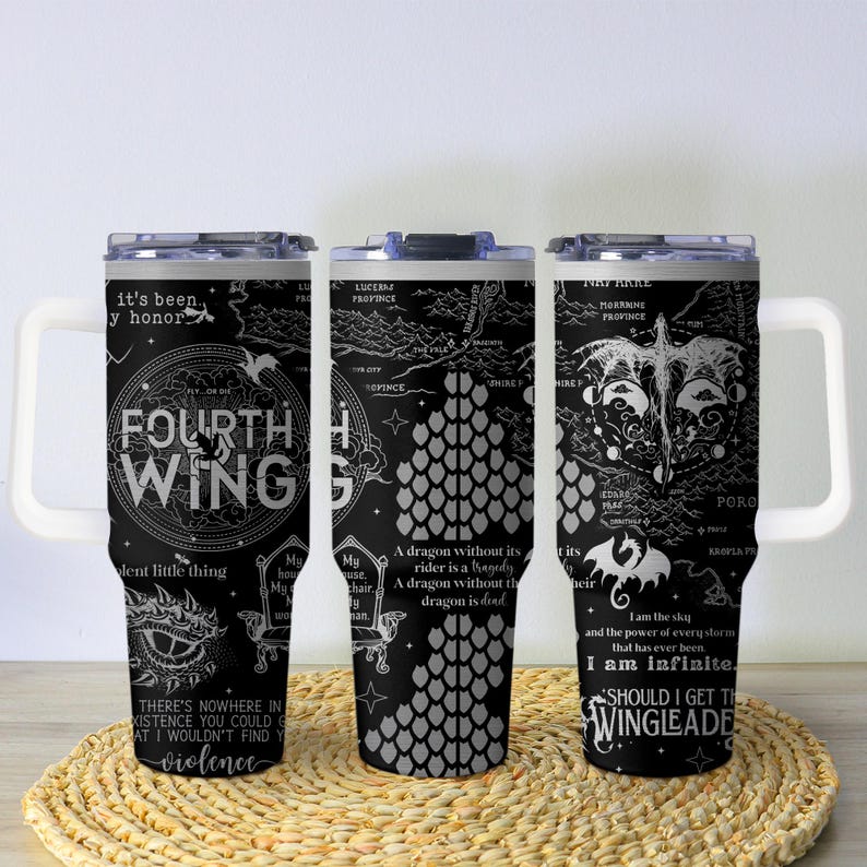 May include: Three black travel mugs with white handles and lids. Each mug features a detailed white graphic design with text, including "FOURTH WING" and dragon illustrations. The mugs are on a woven, circular mat.