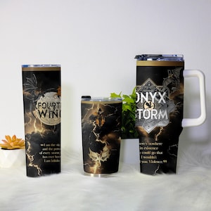 May include: Three black insulated tumblers with dragon and lightning designs. One reads "FOURTH WING", another "ONYX STORM", and the third features a silhouette. The tumblers have black lids and white handles.