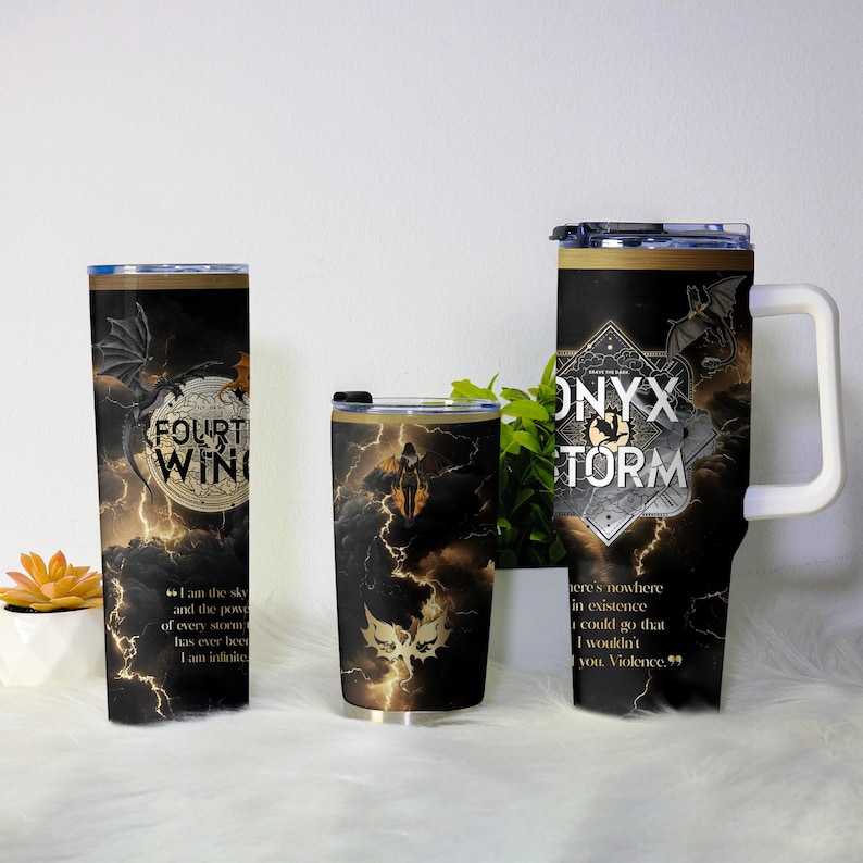 May include: Three black insulated tumblers with dragon and lightning designs. One reads "FOURTH WING", another "ONYX STORM", and the third features a silhouette. The tumblers have black lids and white handles.