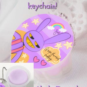 May include: A Jax Pudding Cup keychain with a purple bunny design, stars, and a rainbow. The keychain has a grape-flavored pudding label and the text "Made To Order". The pudding cup is visible.