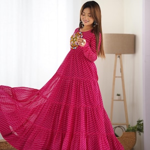 May include: A pink tiered maxi dress with white stripes and a colorful embroidered design on the bodice.