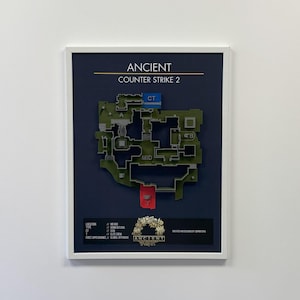 Puede incluir: Impresión enmarcada del mapa "Ancient" de Counter-Strike 2. El mapa es verde con marcadores azules y rojos, etiquetados como "CT", "A", "B" y "MID". El texto "ANCIENT" y "COUNTER STRIKE 2" está en la parte superior.