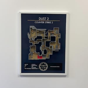 May include: Framed artwork featuring the Dust 2 map from Counter-Strike 2, with a detailed layout in shades of gray and brown. The map is set against a dark blue background, with the text "DUST 2 COUNTER STRIKE 2" at the top. Additional text details the location and type.
