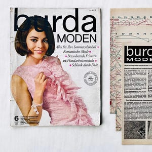 May include: A vintage Burda Moden magazine cover featuring a woman in a pink dress with a ruffled neckline. The magazine cover is from June 1968 and features the text "Burda Moden" and "Alles für Ihre Sommerschönheit".