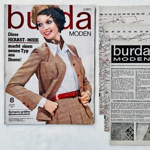 Könnte beinhalten: Ein Vintage-Magazincover mit einer Frau, die einen braunen karierten Blazer und eine weiße Bluse trägt. Das Magazin trägt den Titel "burda MODEN" und der Text "Diese HERBST-MODE macht einen neuen Typ aus Ihnen!" ist auf dem Cover abgedruckt. Das Magazin ist aus dem August 1969.