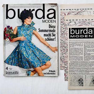 Puede incluir: Una portada de revista vintage con una mujer que lleva un vestido estampado en azul y blanco. La revista se titula "Burda MODEN" y el texto "Diese Sommermode macht Sie schöner!" está impreso en la portada. La portada de la revista también presenta el texto "Europas größte Modenzeitschrift" y "70 Modelle zum Selbermachen".