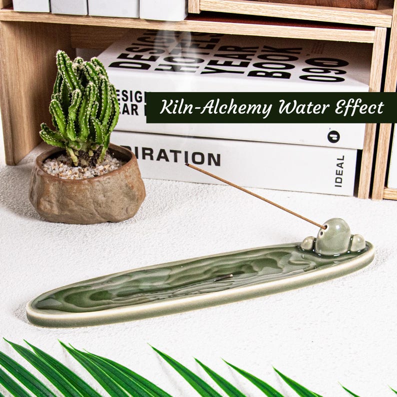 May include: A green ceramic incense holder with a water effect design. The holder has a small, rounded incense stick holder. A small cactus in a brown pot sits to the left. The text "Kiln-Alchemy Water Effect" is visible.