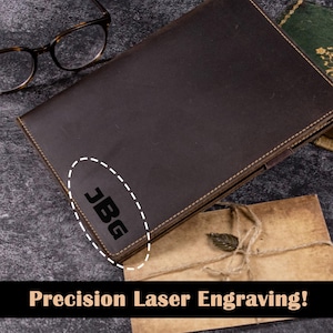 May include: A dark brown leather journal with the initials "JBG" laser engraved. The journal is open, revealing the pages inside. The image also includes a pair of eyeglasses and a small envelope. The text at the bottom reads "Precision Laser Engraving!"