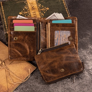 以下が含まれることがあります： 茶色の革製財布。複数のカードスロット、ジッパー付きコンパートメント、独立した小さな小銭入れがあります。財布は開いており、カラフルなカード、現金、運転免許証が見えます。革は使い古したような外観をしています。