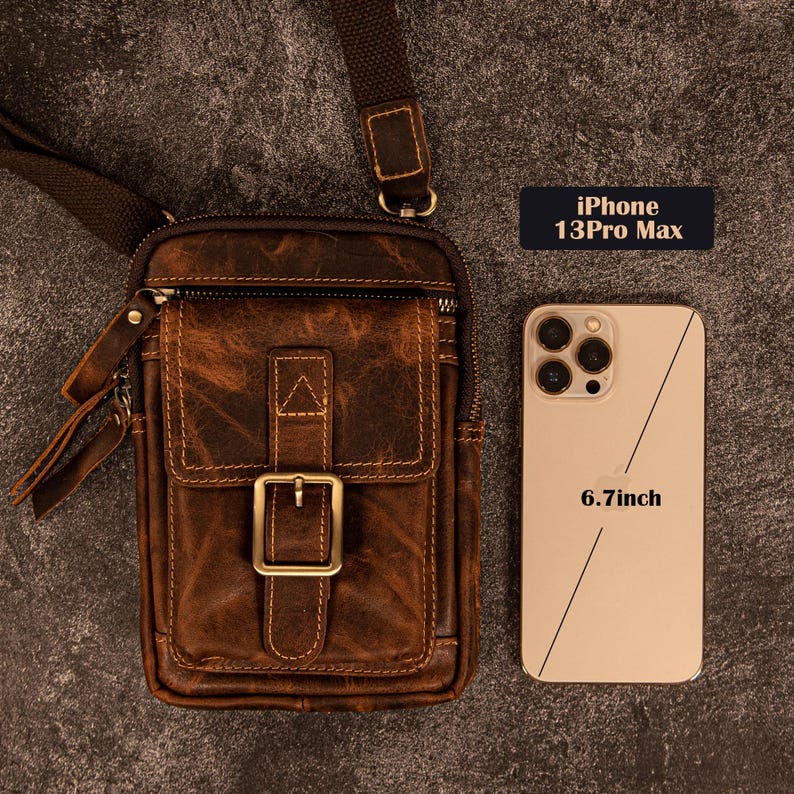 May include: A brown leather crossbody bag with a front flap and buckle closure. The bag is next to a gold iPhone 13 Pro Max with a 6.7-inch screen. The bag has a shoulder strap and a textured appearance.