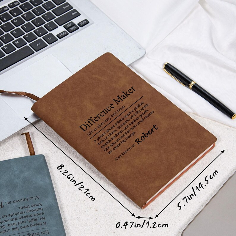 May include: A brown leather journal with the text "Difference Maker" and the name "Robert". The journal is open, showing the pages, and has a ribbon bookmark. Dimensions are 8.26 inches by 5.7 inches by 0.47 inches.