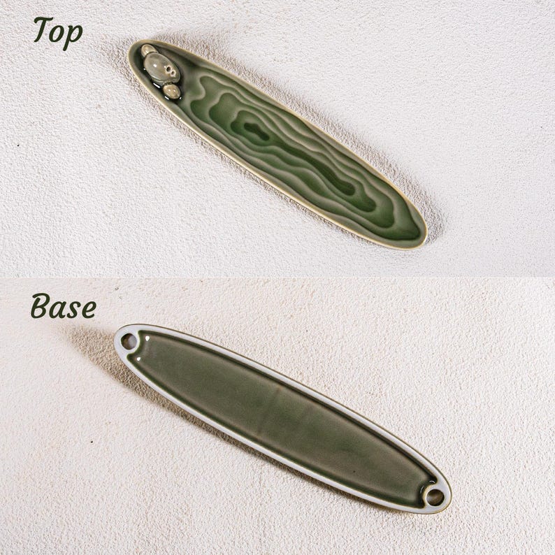 May include: Two views of a ceramic incense holder. The top view shows a long, oval-shaped dish with a green, wood-grain design and a small decorative element. The base view shows the underside of the dish, with a solid green color and two holes.