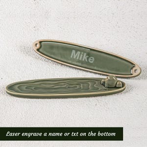 May include: Two green ceramic incense holders. One is engraved with the name "Mike". The other has a textured design and a small decorative element. The text "Laser engrave a name or txt on the bottom" is at the bottom.