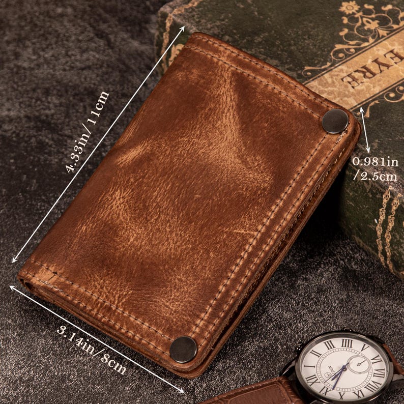 May include: A brown leather wallet with a distressed finish. The wallet is rectangular, measuring 4.33 inches by 3.14 inches and 0.981 inches thick. It features visible stitching and two metal snap closures. A watch with a white face and Roman numerals is visible.