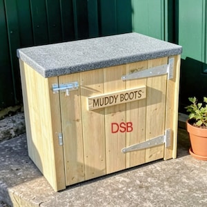 May include: A wooden storage chest with a grey textured top, featuring a metal latch and hinges. A wooden sign attached to the front reads MUDDY BOOTS, and the letters DSB are printed in red below the sign on the vertical wooden planks.
