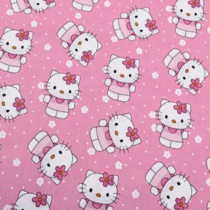 Peut inclure: Tissu rose avec un motif répété du personnage Hello Kitty. Chaque personnage est blanc avec une fleur rose, portant une robe rose. Le fond est rose uni avec de petites formes de fleurs blanches.