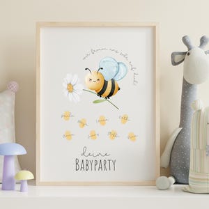 May include: A framed print featuring a cartoon bee holding a daisy, with the text "deine BABYPARTY". The bee has yellow and black stripes and blue wings. Names are written below the bee in yellow circles. The frame is light wood.