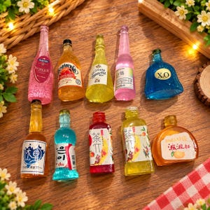 Op de afbeelding: Een verzameling van tien decoratieve miniatuurflesjes in verschillende vormen en kleuren, waaronder roze, oranje, geel, blauw en helder glas. De flesjes zijn voorzien van diverse etiketten met tekst zoals Martell, Sundaberg, Casa, X.O en diverse Aziatische tekens.
