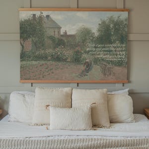 May include: A bedroom scene featuring a bed with white bedding and several cream-colored pillows. Above the bed hangs a framed landscape painting with text that reads "Make it your ambition to live quietly and peacefully, and to mind your own affairs and work with your hands."