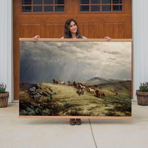 May include: A large framed print of a painting depicting a herd of horses running across a grassy hillside under a stormy sky. The artwork features a landscape with a mountain in the background and a wooden frame.