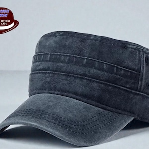 May include: A dark gray, weathered-look military-style cap with a short brim. The cap features horizontal stitched details across the crown and a curved brim. The image includes a logo with text that reads "UNIQUE DESIGNS HAT / CAPS".