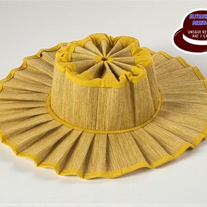 Puede incluir: Un sombrero de sol amarillo de ala ancha con un diseño plisado. El sombrero presenta una textura tejida y un ribete amarillo en contraste. El sombrero tiene el texto "ELIYASHEV BRINSON UNIQUE DESIGNS HAT / CAPS" en un logotipo.