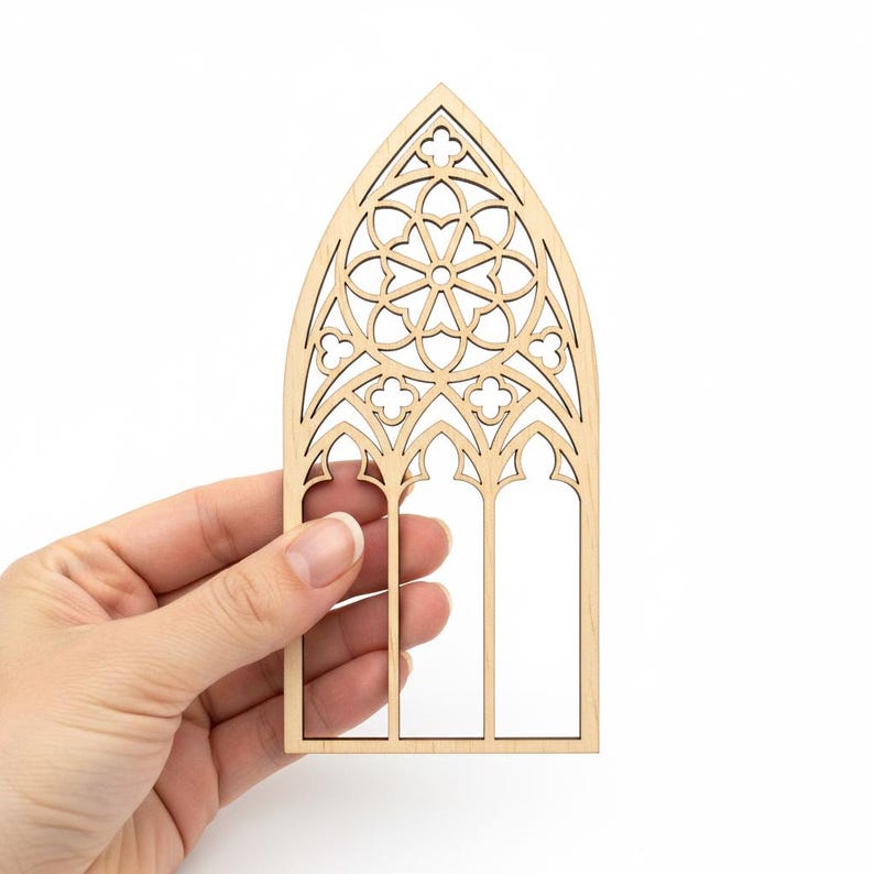 May include: A laser-cut wooden gothic window with intricate floral and geometric patterns. The window features a pointed arch and three vertical sections, with a central rose window design. The natural wood color provides a neutral tone.