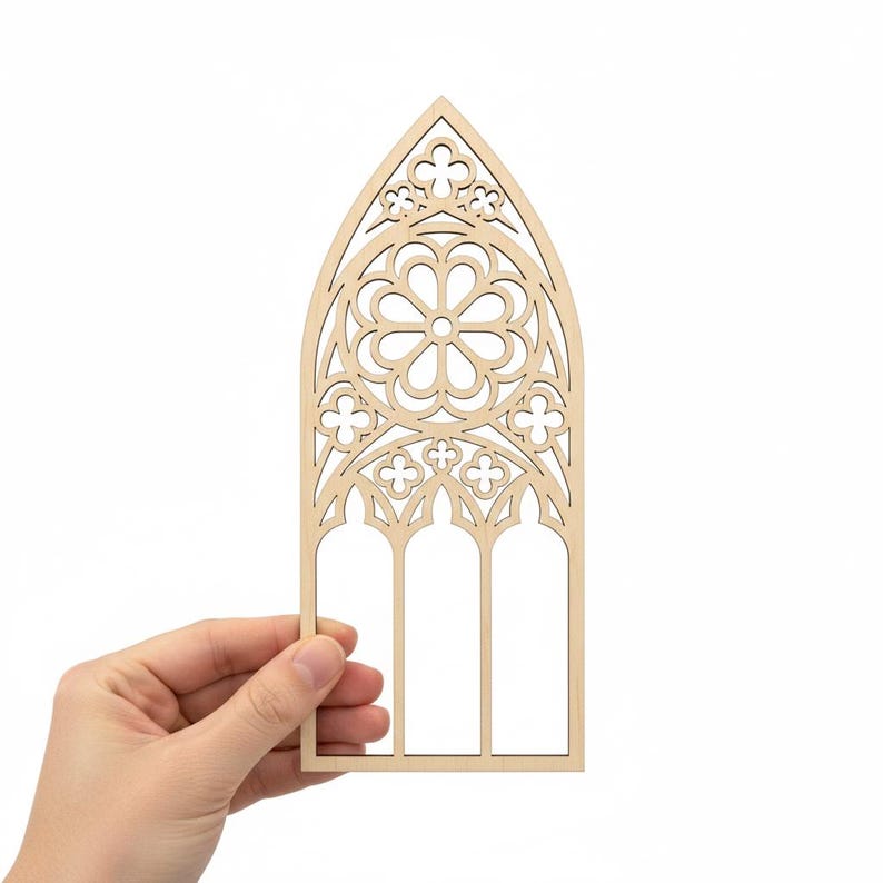 May include: A laser-cut wooden gothic window design. The window features a central floral pattern, trefoil details, and three arched panels. The natural wood color provides a neutral base for crafting or decoration. The window is held by a hand.