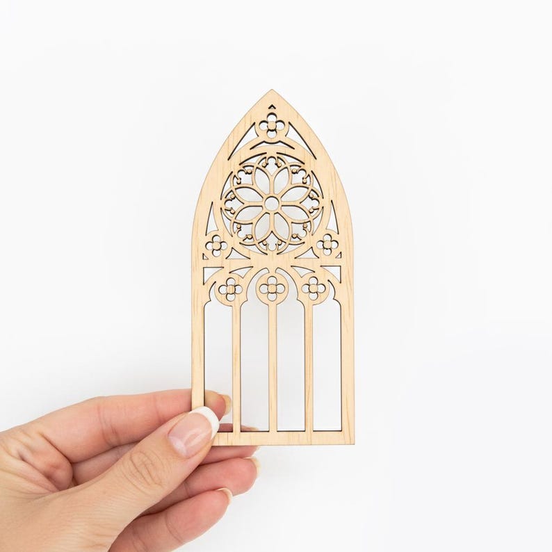 May include: A laser-cut wooden gothic window design. The window features an arched top with intricate floral and geometric patterns. The natural wood color provides a neutral tone, suitable for various craft projects or home decor.