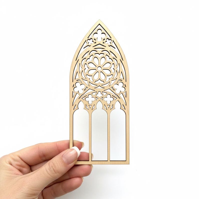 May include: A laser-cut wooden window frame with an arched top and intricate floral and geometric designs. The frame features three vertical rectangular openings and is held against a white background.