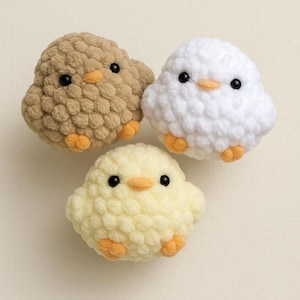 May include: Three crocheted chick toys. One is brown, one is white, and one is yellow. Each chick has black eyes, an orange beak, and orange feet.