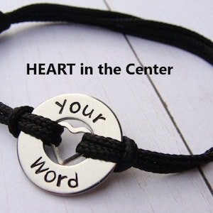 May include: Black cord bracelet with a silver charm that says "Your Word" with a heart cut out in the center. The charm is attached to the cord with a knot.