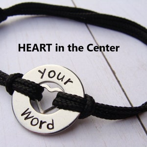 May include: Black cord bracelet with a silver charm that says "Your Word" with a heart cut out in the center. The charm is attached to the cord with a knot.