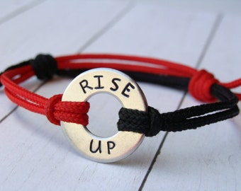 May include: A red and black braided bracelet with a silver charm that says "RISE UP".