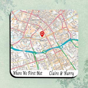 May include: Square coaster with a map of Manchester, England, marked with a red heart. The text "Where We First Met Claire & Harry" is printed below. The coaster has a black border and is a unique keepsake.