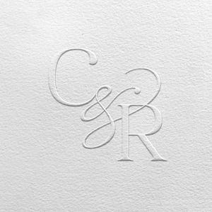 May include: White embossed monogram featuring the letters C, S, and R in a stylized script. The letters are raised against a textured white background, creating a subtle, elegant design. The overall aesthetic is clean and minimalist.