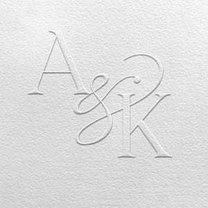 May include: Monogram design featuring the letters A, S, and K in a delicate, intertwined script. The letters are embossed on a textured, off-white paper, creating a subtle, elegant effect. Ideal for wedding invitations or stationery.