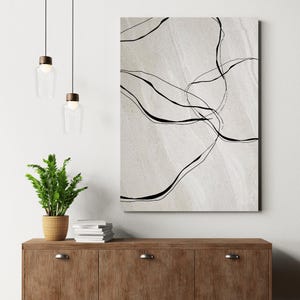 May include: A black and white abstract art print with a white background and black lines forming abstract shapes. The print is hanging on a white wall above a wooden cabinet.