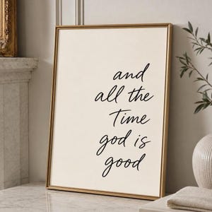 Può includere: Una stampa artistica da parete rettangolare in una sottile cornice dorata con testo nero in corsivo su sfondo color crema che recita: and all the Time god is good. La stampa è orientata verticalmente e presenta un design pulito ed elegante.
