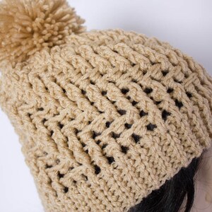May include: A beige crocheted beanie with a fluffy pom pom on top.