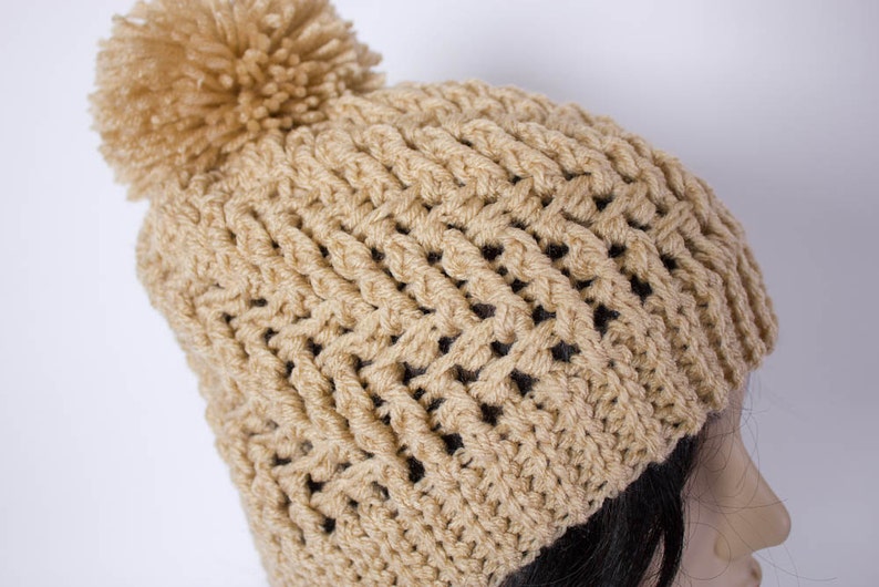 May include: A beige crocheted beanie with a fluffy pom pom on top.