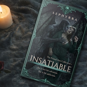 Paperback book titled Insatiable by Sephyrra resting on dark fabric with a lit candle and red rose beside it in a moody gothic setting.