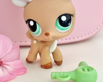 May include: A tan deer figurine with large, expressive eyes, white spots, and a small green accessory. The deer has large, white-tipped ears and is posed in a standing position. The accessory is a small, green toy.