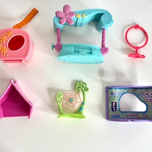 Puede incluir: Colección de coloridos accesorios de juguete de plástico, que incluyen un estuche rosa con correa naranja, un columpio azul con una flor, un collar rosa, una tienda de campaña rosa, una estructura verde similar a una telaraña y una habitación morada con espejo.