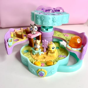 May include: A colorful toy playset featuring miniature animal figures. The playset has a flower-shaped design with a rotating top and various themed areas, including a farm scene and a slide. The toy is made of plastic and has a variety of colors.