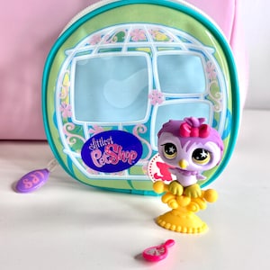 May include: A Littlest Pet Shop owl figurine with a pink bow, perched on a yellow stand, next to a pink mirror and a round green and blue case. The case has the words "Littlest Pet Shop" on it.